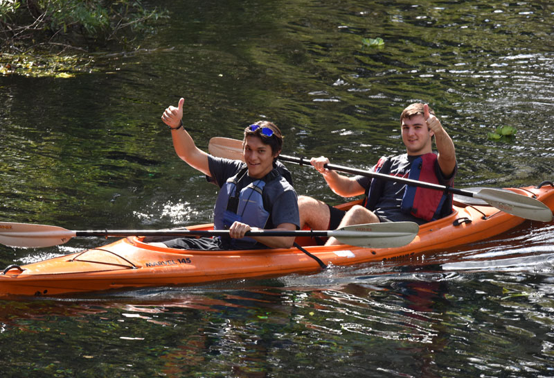 Student kayaking and giving thumbs up
